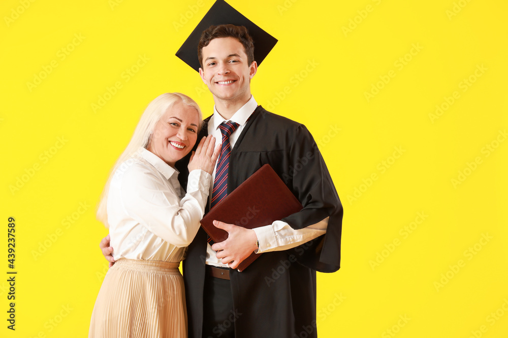 Happy male graduation student with his mother on color background
