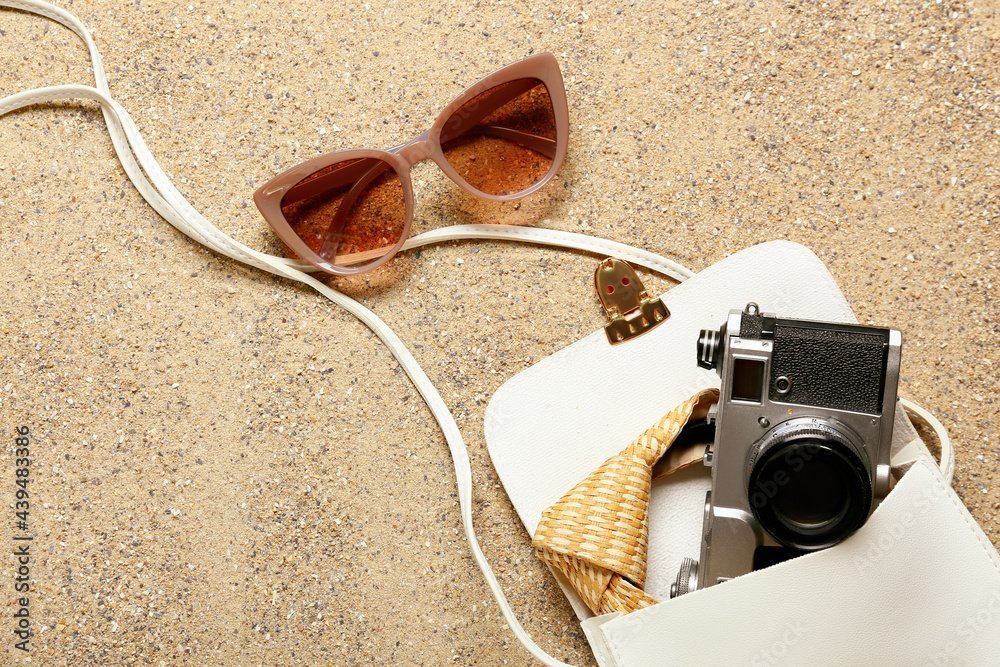 Stylish sunglasses with bag and photo camera on sand