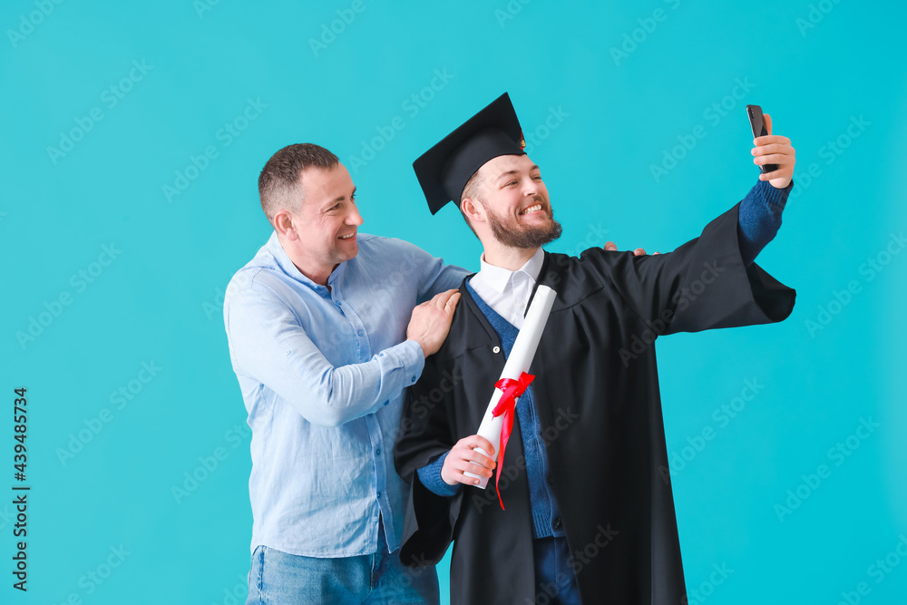 快乐的男毕业学生和他的父亲在彩色背景上自拍