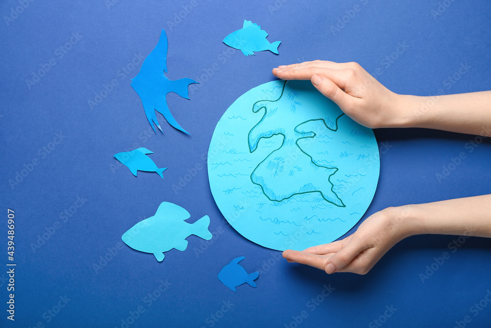 人类的手与纸行星地球和彩色背景上的鱼类。生态学概念
