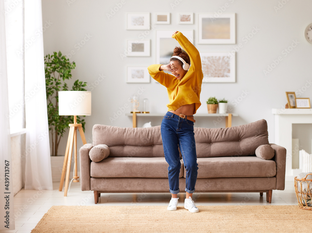 年轻顽皮的非裔美国妇女戴着耳机在家里的客厅里蹦蹦跳跳