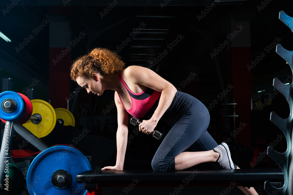 一位魅力四射的年轻女子在健身房练习哑铃。