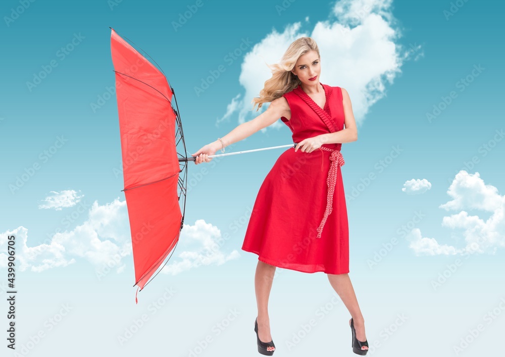 Composition of woman in red dress standing with inside out umbrella against cloudy blue sky