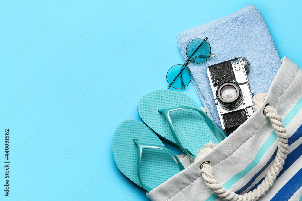 Bag with beach accessories on color background