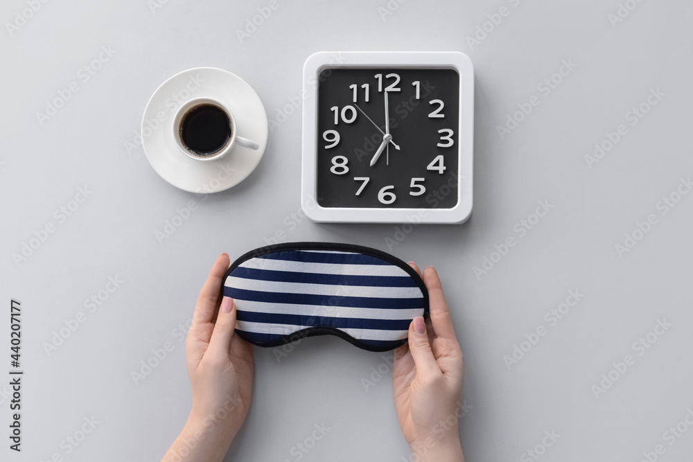 女性双手，带睡眠面罩，一杯咖啡，灰色背景时尚时钟