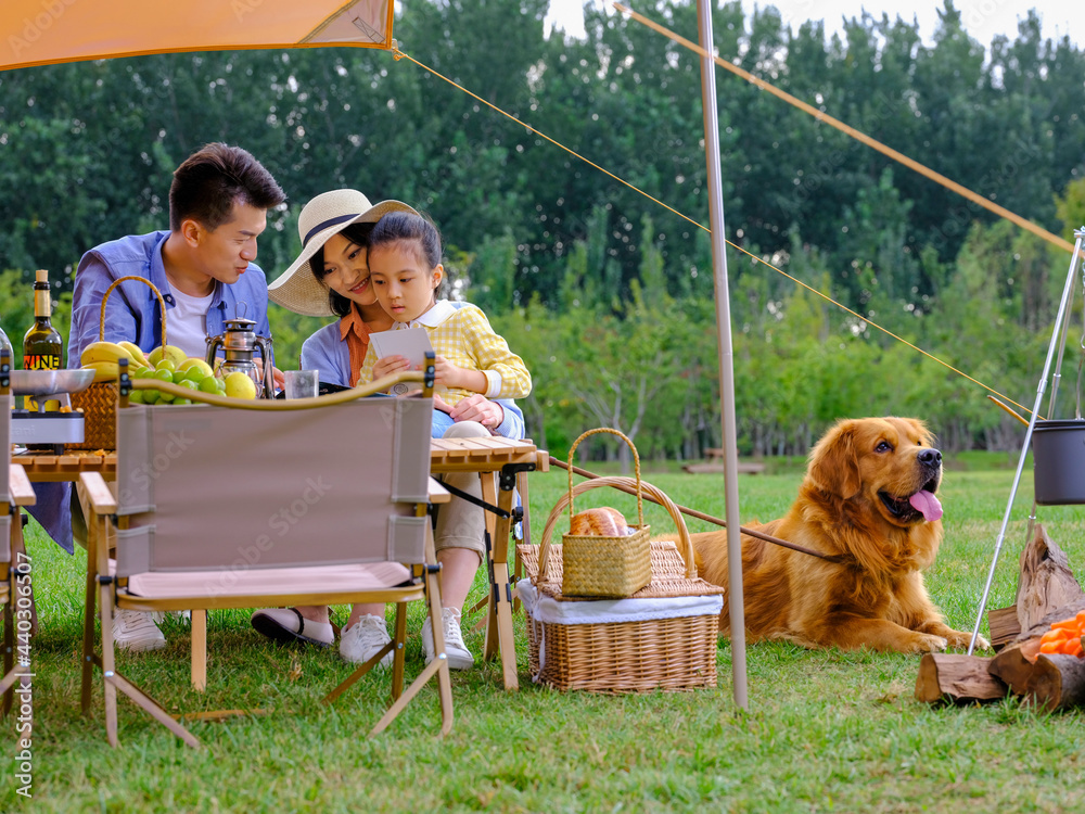 Happy family of three and pet dog reading outside