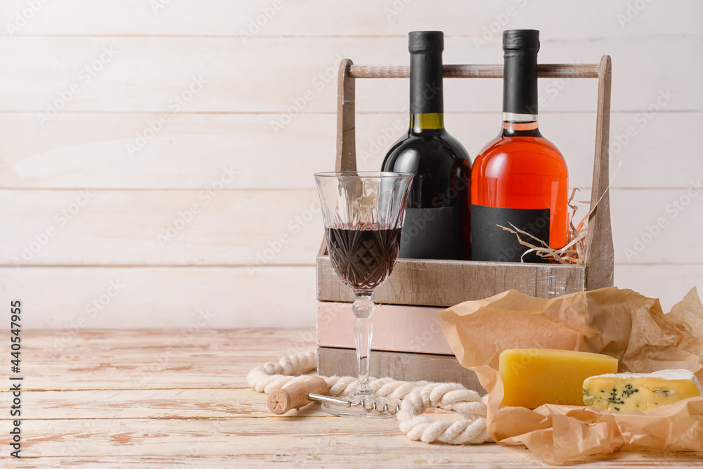 浅木背景上装有葡萄酒、奶酪和玻璃杯的盒子