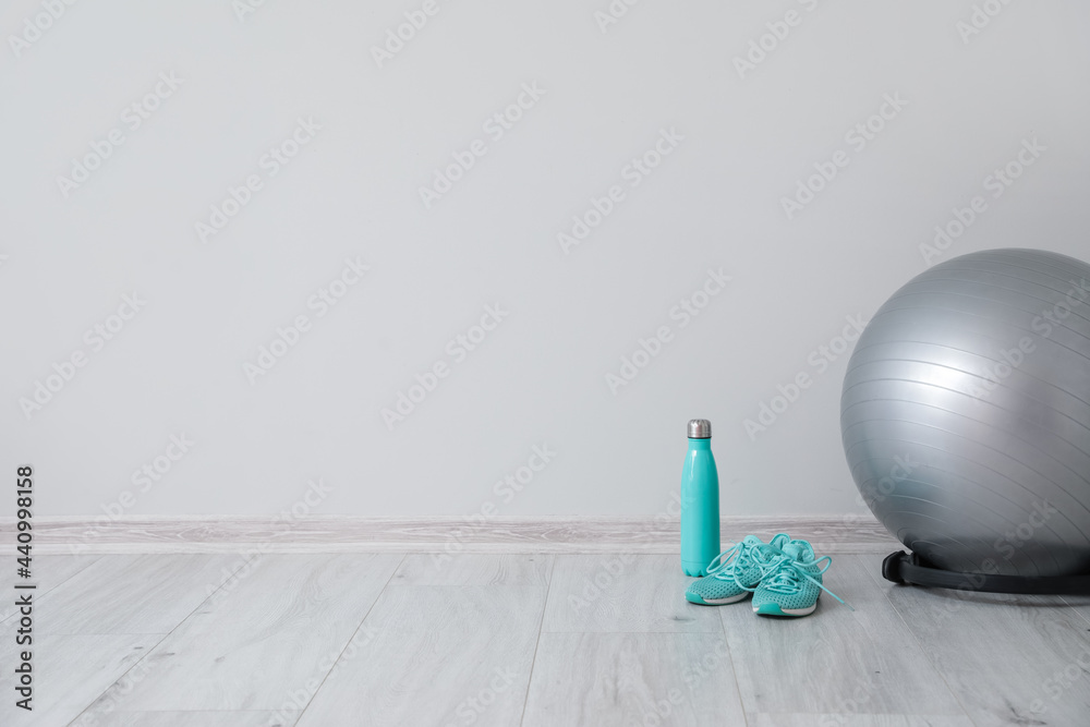 Fitness ball, bottle and shoes near light wall