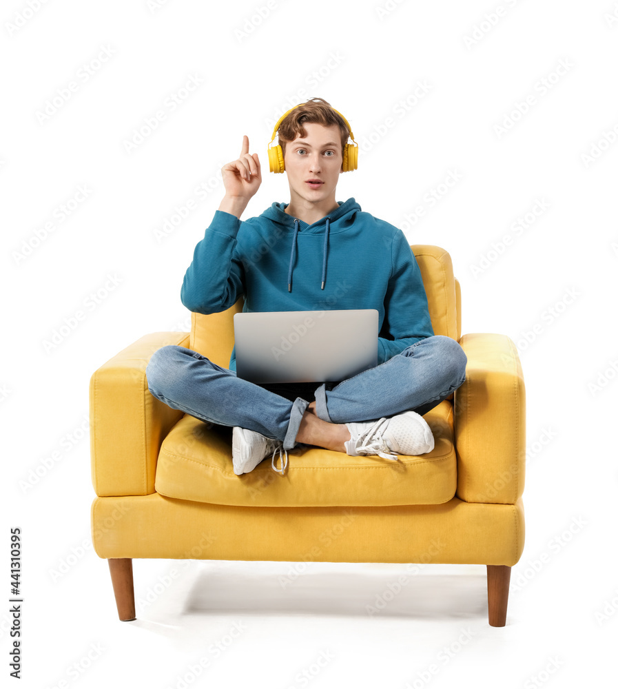 一个年轻人，拿着笔记本电脑，竖起食指，坐在白色扶手椅上听音乐