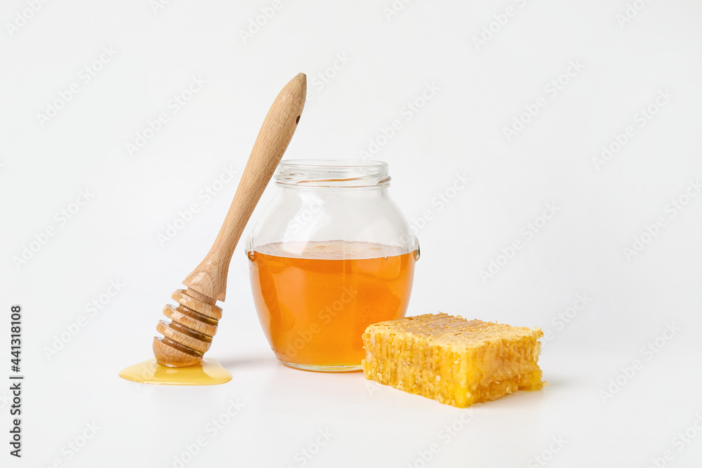 白底甜蜂蜜、勺子和梳子的玻璃罐