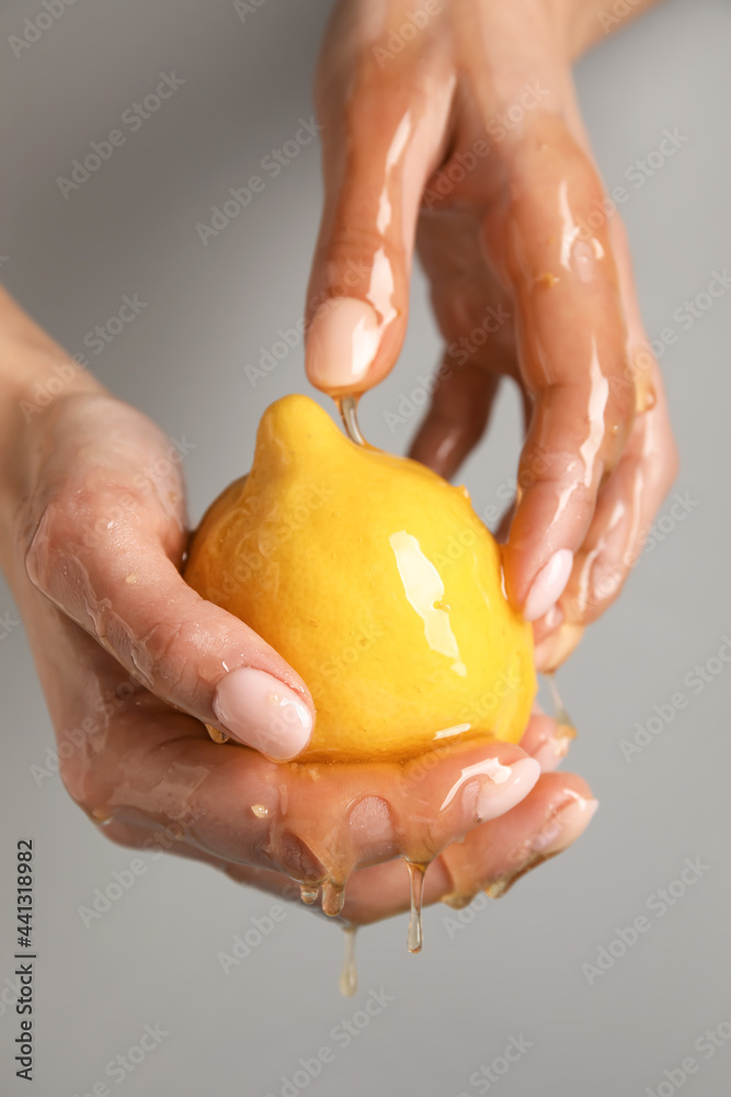 灰色背景下，女性双手拿着成熟的柠檬和滴着的蜂蜜，特写
