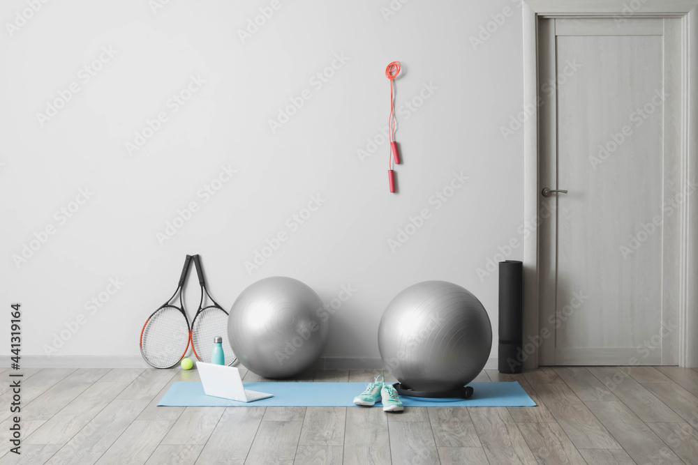 Different sports equipment with fitness balls and modern laptop near light wall