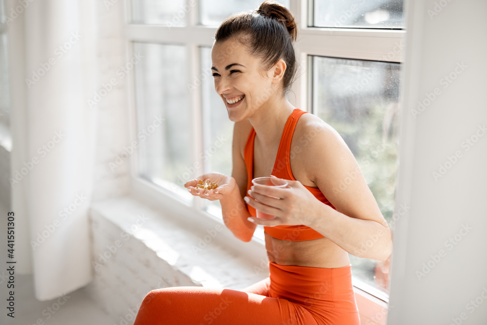 快乐女人在健身房训练后服用胶囊形式的补充剂或维生素。概念