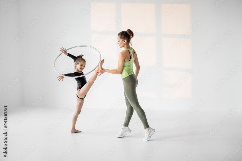 年轻妈妈或体育教练在白色课堂上用跳绳训练小女孩进行艺术体操