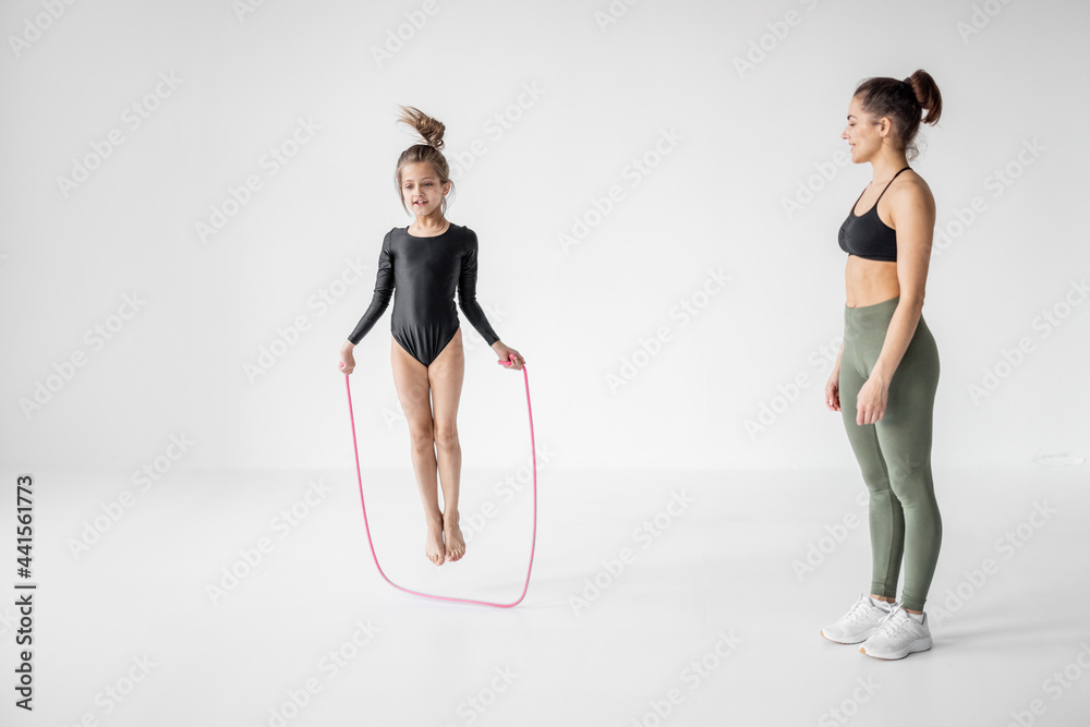 年轻的妈妈或体育教练在白色课堂上用跳绳训练小女孩进行艺术体操