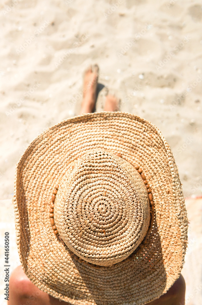 Summer holiday fashion concept - tanning woman wearing sun hat at the beach on a white sand shot fro
