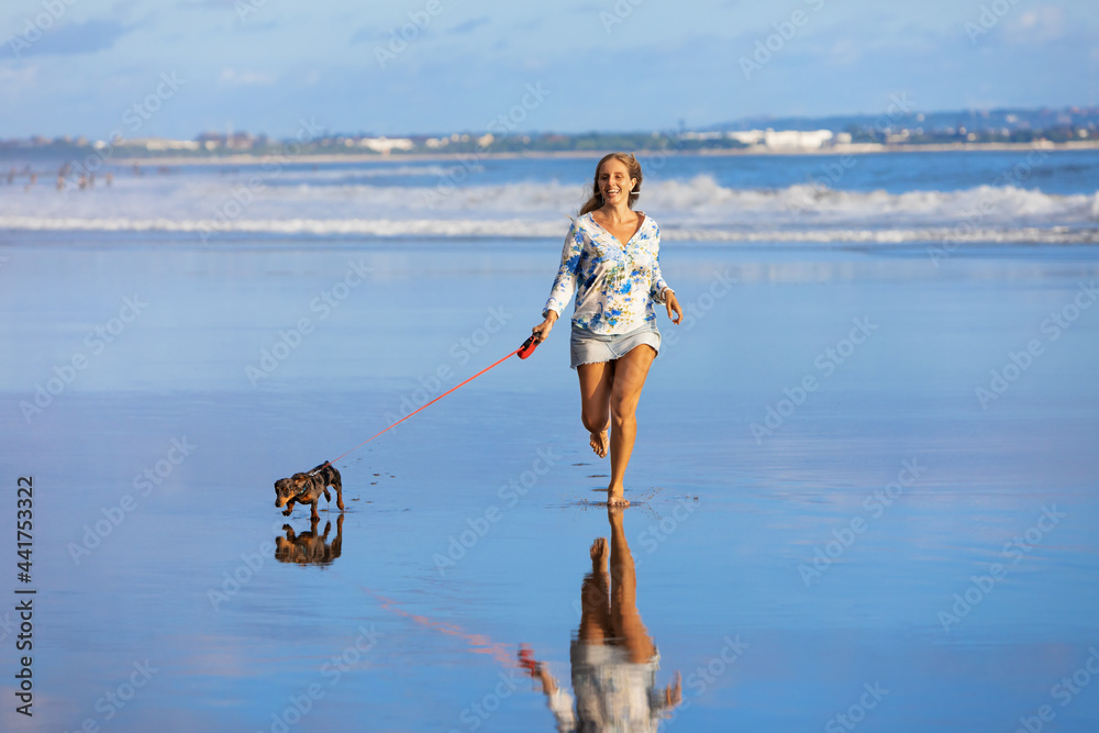 年轻快乐的女孩和达克斯猎犬玩得很开心，沿着沙滩上的海浪，在水池边奔跑。Beauti