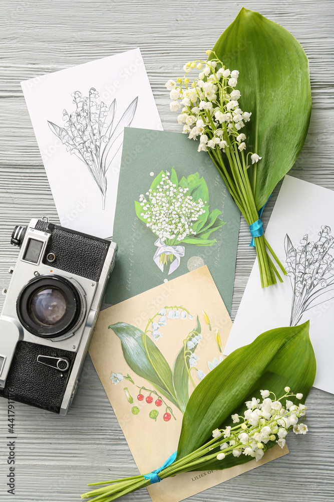 美丽的铃兰花、相机和浅色木质背景的贺卡