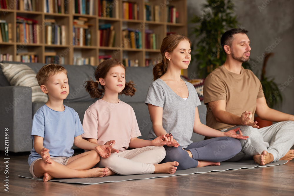 Father, mother and two kids sitting in lotus pose on floor and meditating with closed eyes