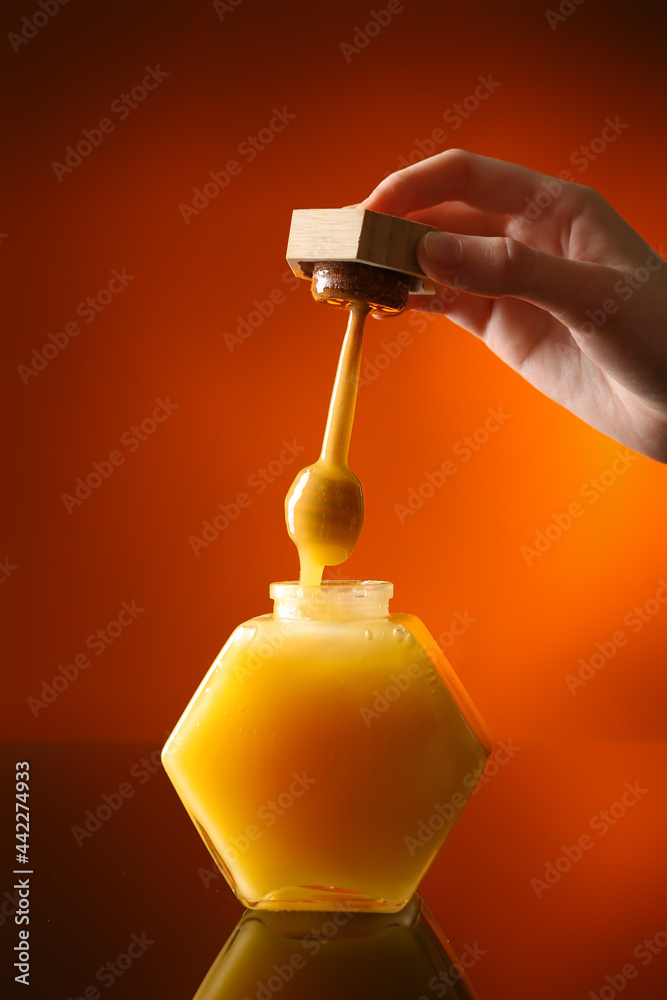 一名妇女将蜂蜜从勺子中倒入彩色背景的玻璃罐中