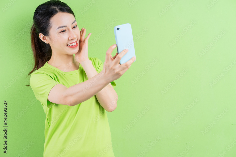 年轻的亚洲女性在绿色背景下使用智能手机