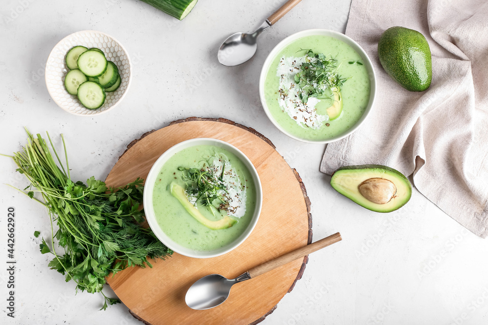 Bowls with green gazpacho and ingredients on light background