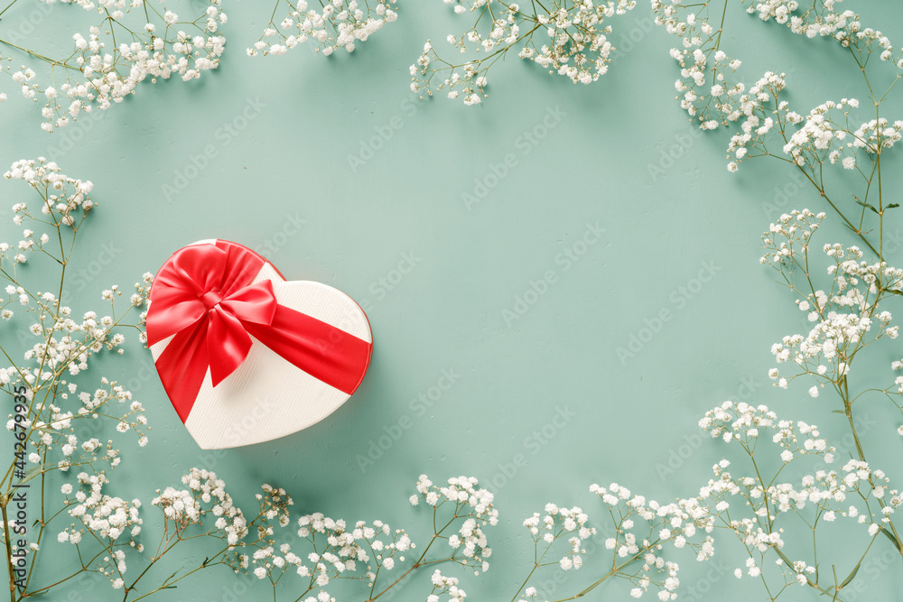 带礼物的鲜花组合。绿松石蓝色背景上的白花和成形的心形礼物。周三