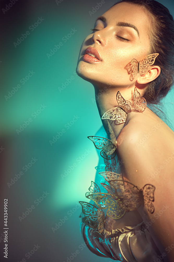 Beauty model girl in colorful bright neon lights posing, fashion make up with butterfly. Portrait of