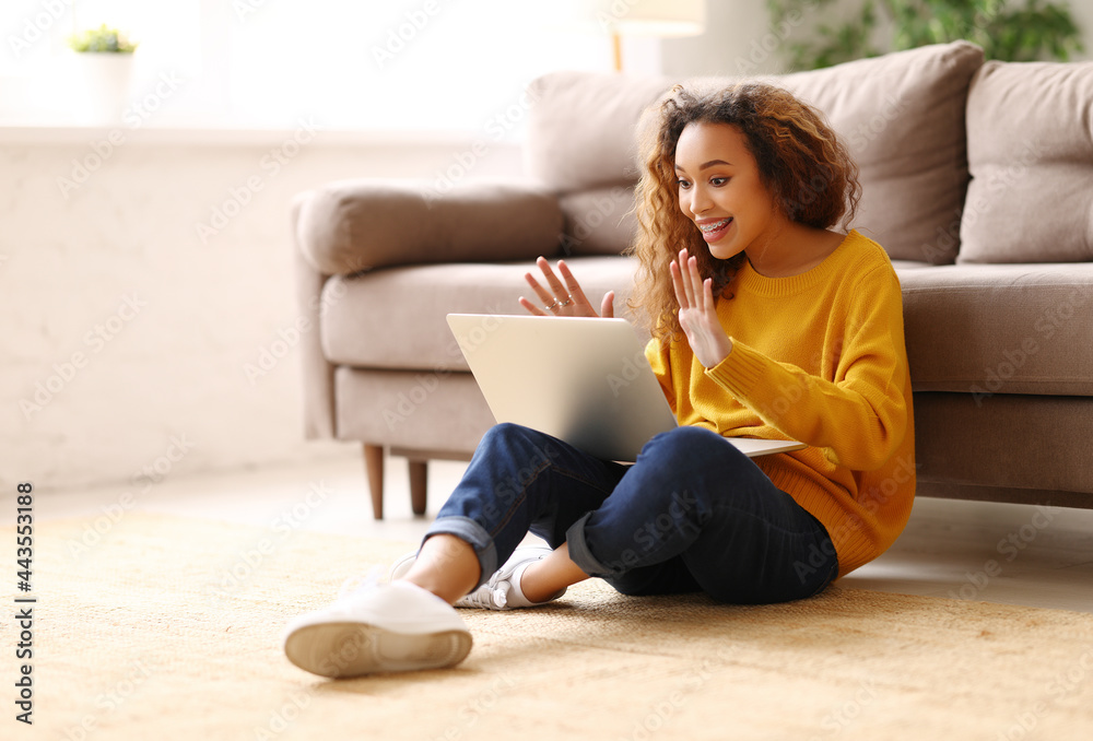 惊讶的非裔美国女性在家里的沙发上在线工作或学习时进行视频通话
