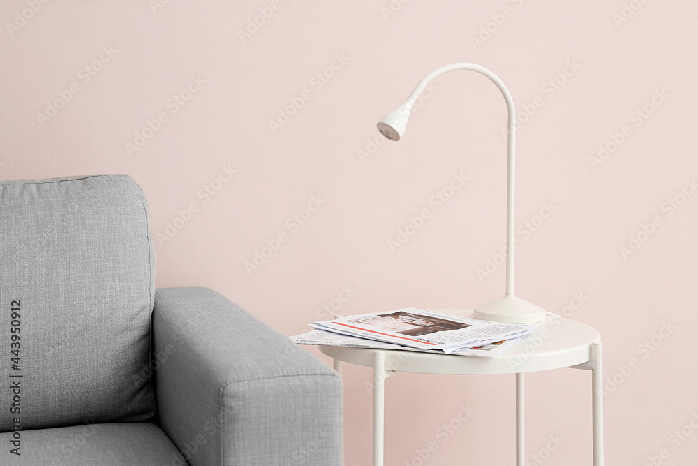 Modern lamp and newspapers on table near color wall