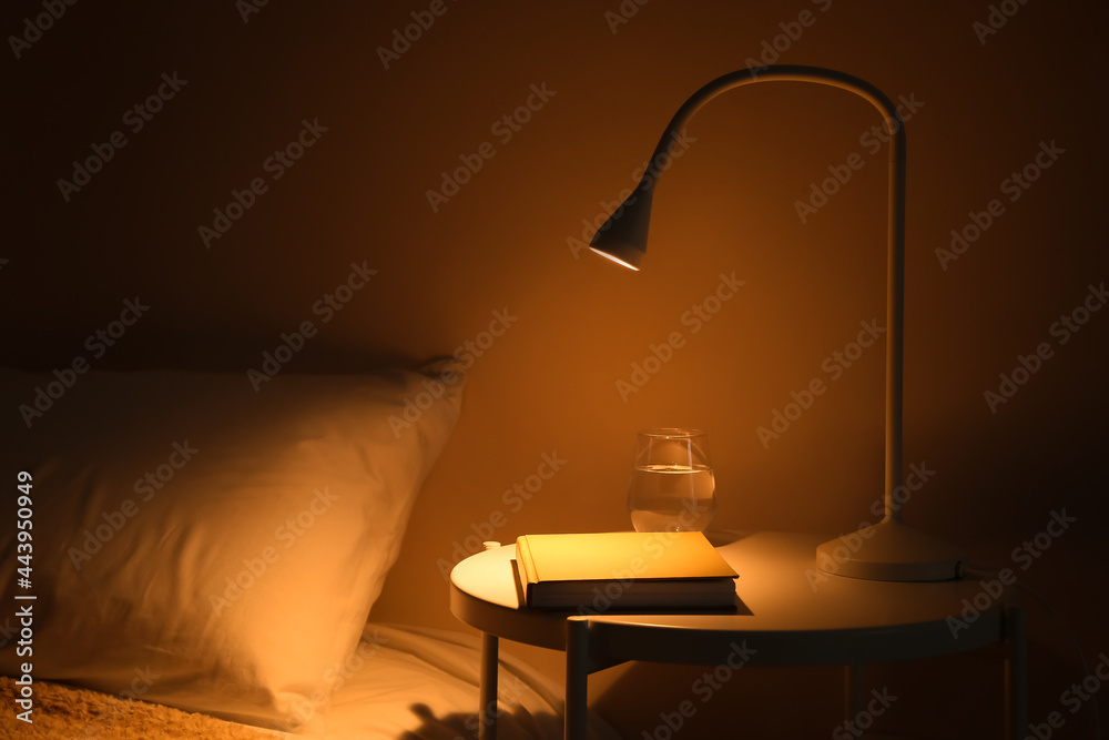 在黑暗的卧室里发光的灯和桌子上的书