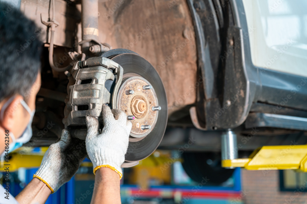 汽车修理工在汽车修理厂检查被举升汽车的车轮制动盘和制动蹄