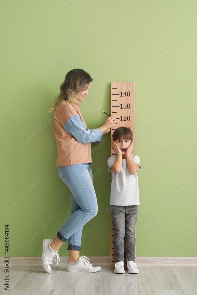 一名妇女在彩色墙附近测量小儿子的身高