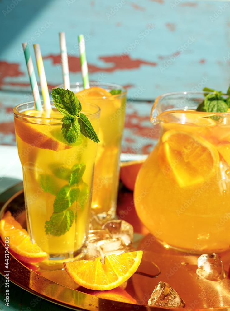 Glasses of lemonade with lemons, oranges and mint leaves on blue wooden background. Summer cold drin