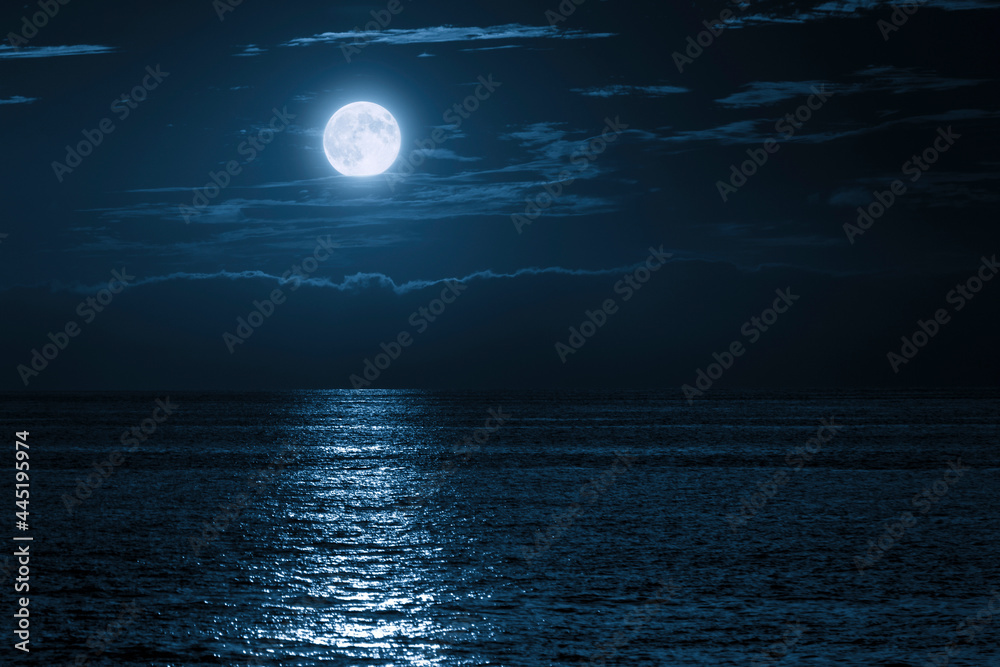 这轮蓝色的满月在平静的海洋中明亮地升起在云层之上