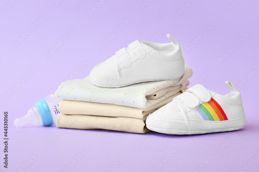 彩色背景上的婴儿衣服、奶瓶和鞋子的堆叠