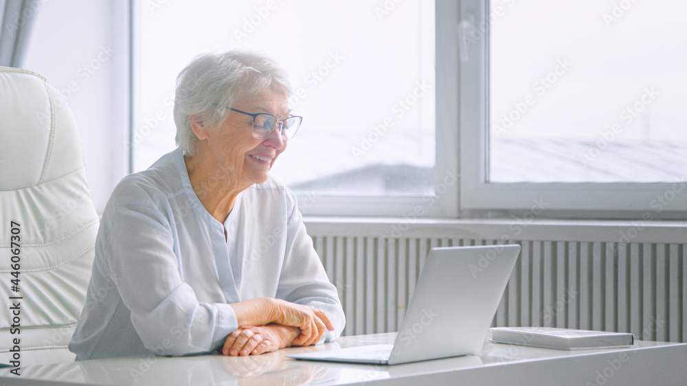 留着灰色发型的老妇人公司经理坐在白色的网上会议上与员工交谈