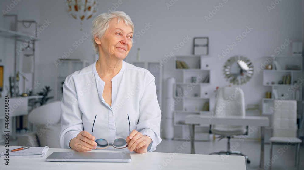 疲惫的白发高级女商人坐在家里合上笔记本电脑，摘下眼镜