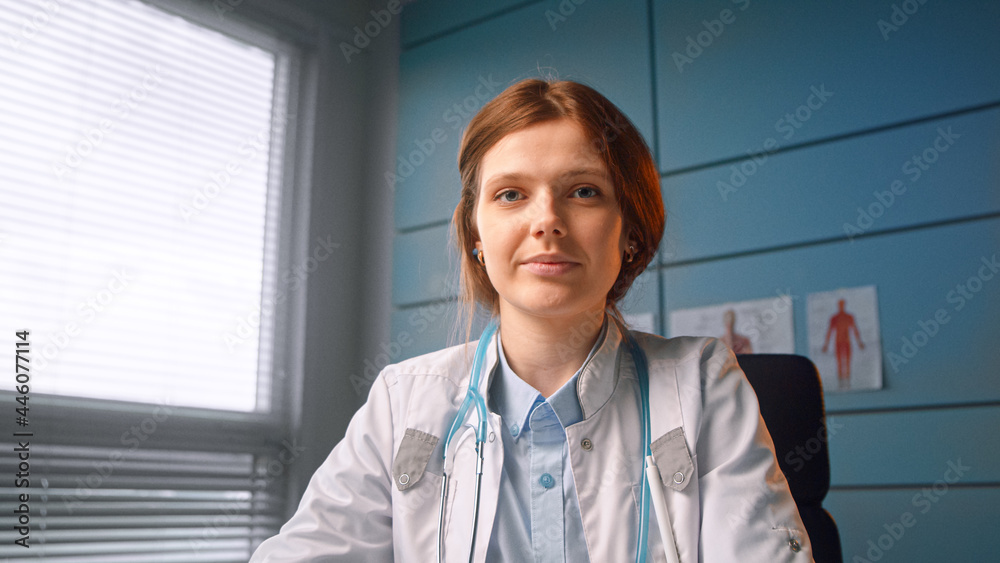 穿着白大褂的严肃女医生在网上会议上坐在椅子上对着蓝色w与患者交谈