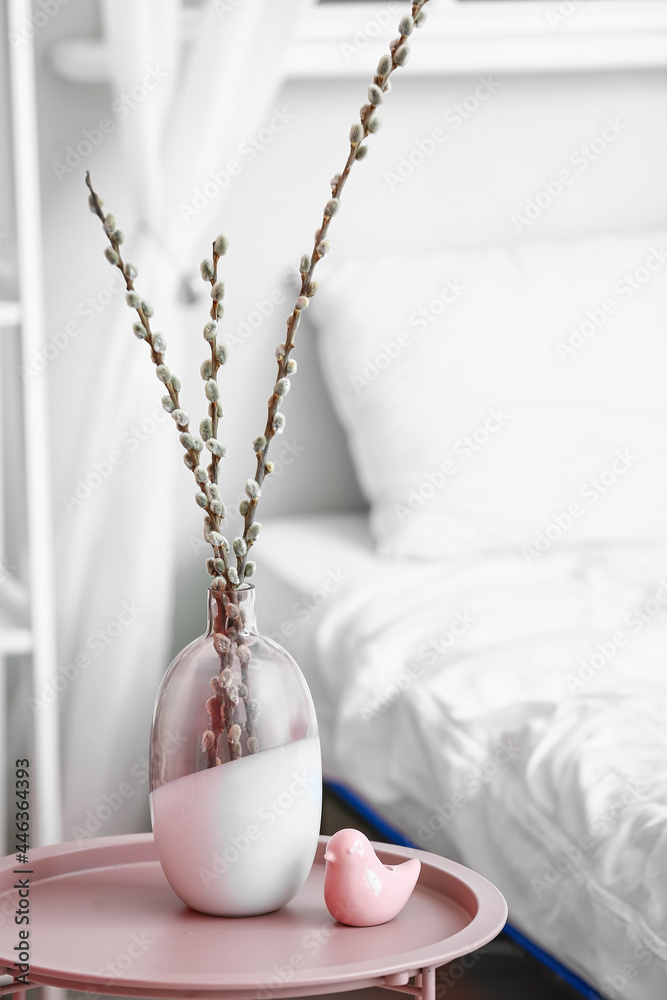 房间靠近床的桌子上有柳树枝的花瓶