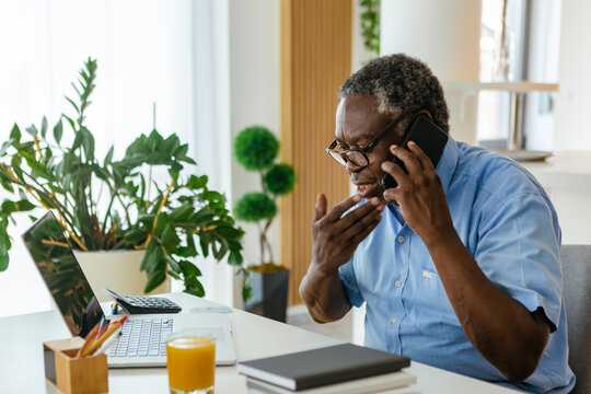 一位非洲高级男子坐在家里的办公室里，正在和保险公司通电话