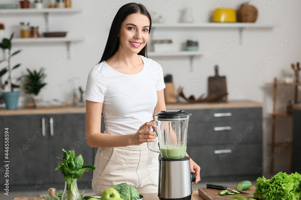 Young woman preparing healthy green smoothie in kitchen