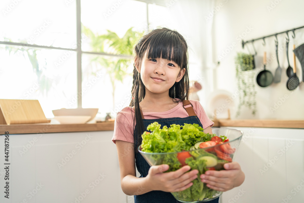 亚洲女孩拿着蔬菜看着厨房里的相机的肖像。