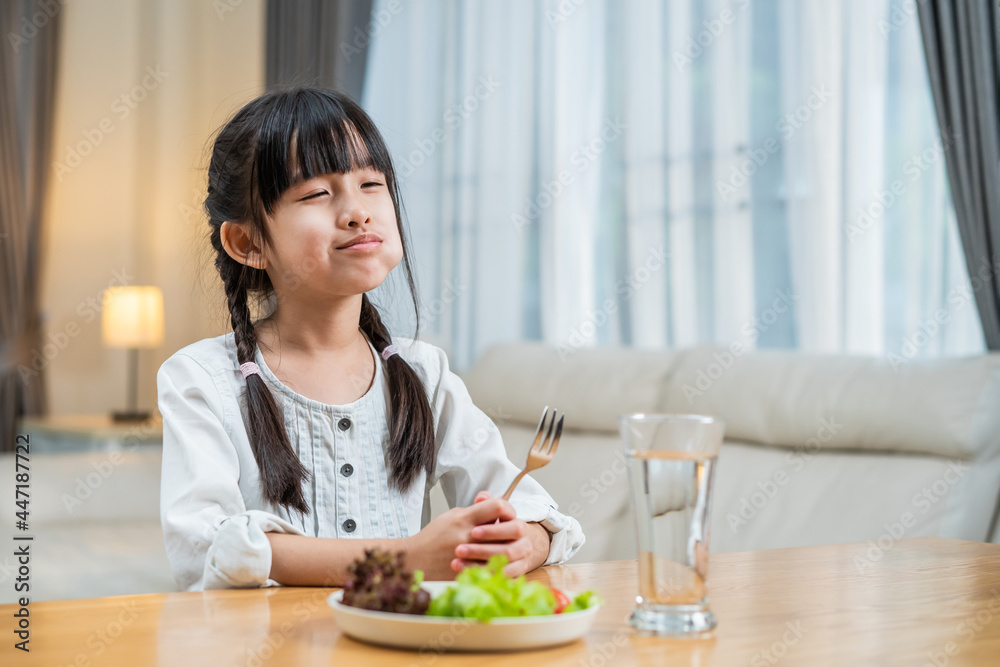 亚洲小女孩在餐桌上吃盘子里的绿色蔬菜。