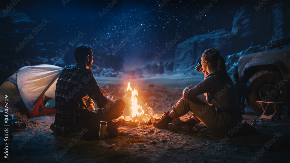 快乐情侣在峡谷露营时坐在篝火旁看夜空。两个旅行的人