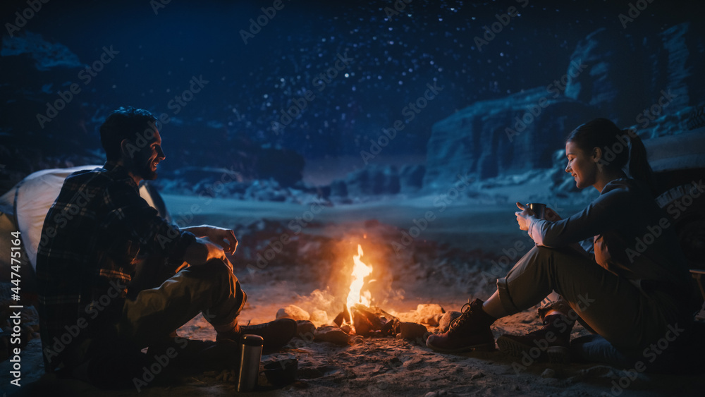 快乐情侣坐在篝火旁看夜空，在峡谷露营。两个旅行的人