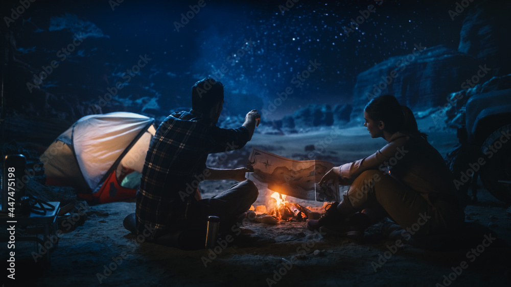 快乐的徒步情侣晚上一起在峡谷露营，坐在篝火旁，计划徒步旅行