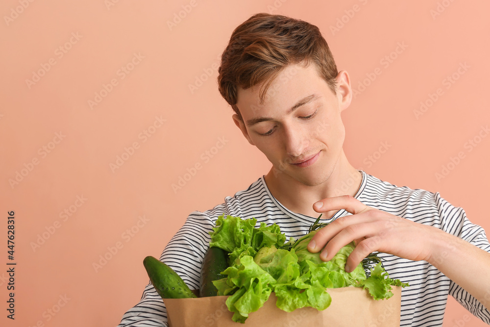 年轻人拿着纸袋，纸袋里有彩色背景的新鲜蔬菜