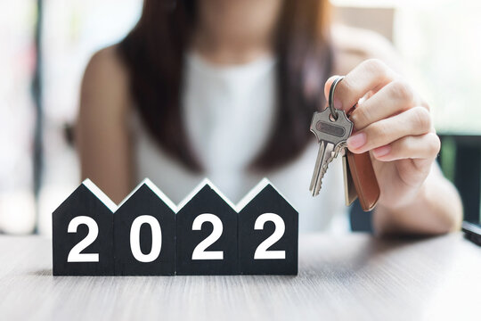 年轻的女商人手握钥匙和2022年新年快乐，房子模型在桌子上的办公室。新