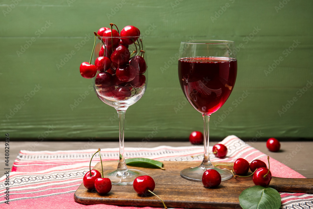 彩色木质背景上的一杯葡萄酒和甜樱桃